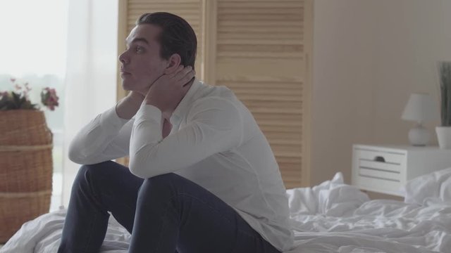 Depressed young man alone at home or hotel room. The guy falling on his bed, he is sad, tired and exhausted. Mental injury, disorder, bad mood. Side view