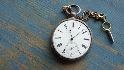 Old, silver and gold pocket watch with wind up key on weathered blue wooden background. Abstract...