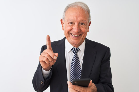 Senior grey-haired businessman using smartphone standing over isolated white background surprised with an idea or question pointing finger with happy face, number one - Powered by Adobe