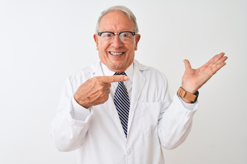 Senior grey-haired scientist man wearing coat standing over isolated white background amazed and smiling to the camera while presenting with hand and pointing with finger.