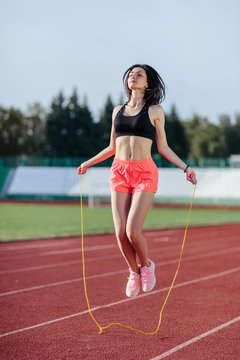 Achieving best results. Beautiful young brunette woman in sports clothing skipping rope and smiling while exercising on the running track outdoors