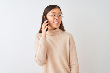 Young chinese woman talking on the smartphone over isolated white background looking away to side with smile on face, natural expression. Laughing confident.