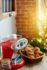 Coffee mashine with croissant, fir branches and Christmas decorations on wooden table in the kitchen. Cozy homely scene, danish hygge concept.