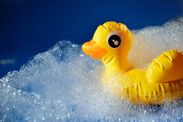 Rubber yellow duck toy on a blue background in foam. Personal hygiene