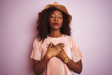 Young african american woman wearing t-shirt and hat over isolated pink background smiling with...