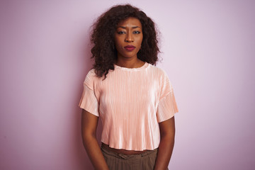Young african american woman wearing t-shirt standing over isolated pink background skeptic and...