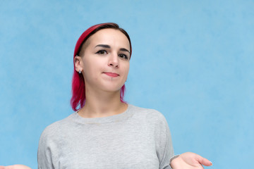 Portrait of the chest of a pretty girl with red hair on a blue background in a gray jacket. Standing in the studio right in front of the camera with emotions, talking, showing hands, smiling