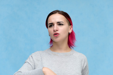 Fototapeta premium Portrait of the chest of a pretty girl with red hair on a blue background in a gray jacket. Standing in the studio right in front of the camera with emotions, talking, showing hands, smiling
