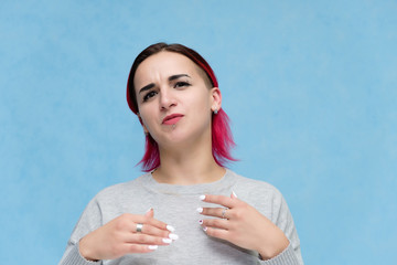 Portrait of the chest of a pretty girl with red hair on a blue background in a gray jacket. Standing in the studio right in front of the camera with emotions, talking, showing hands, smiling