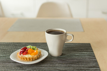 Cake with cream, raspberries, kiwi and orange and a cup of coffee on a black napkin. Pastry with fruits on top. Morning coffee. Copy space.