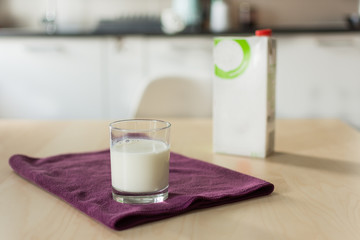 A glass of milk with napkin and paper bottle on wooden table over blur white kitchen background. Blank paper container with milk for design. Organic milk concept.