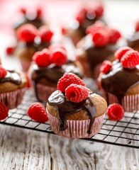 Raspberry muffins with melted dark chocolate and fresh raspberries on  cooling tray on a wooden white table, close up.  A delicious dessert or breakfast
