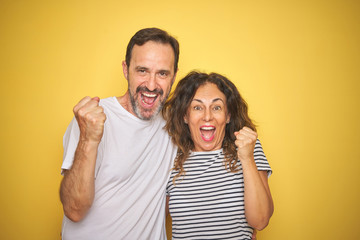 Beautiful middle age couple together standing over isolated yellow background screaming proud and celebrating victory and success very excited, cheering emotion