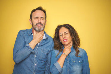 Beautiful middle age couple together standing over isolated yellow background Touching painful neck, sore throat for flu, clod and infection