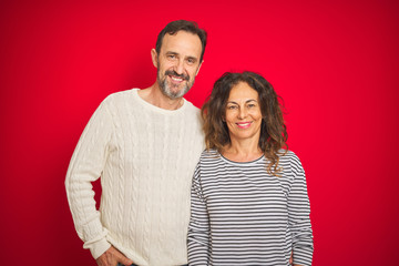 Beautiful middle age couple wearing winter sweater over isolated red background with a happy and cool smile on face. Lucky person.