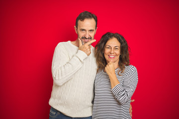 Beautiful middle age couple wearing winter sweater over isolated red background looking confident at the camera with smile with crossed arms and hand raised on chin. Thinking positive.