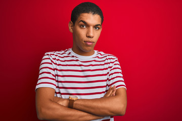 Young handsome arab man wearing striped t-shirt over isolated red background skeptic and nervous,...