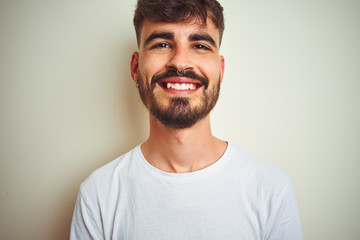 Young man with tattoo wearing t-shirt standing over isolated white background with a happy and cool smile on face. Lucky person.