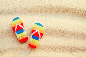 Vacation background with bright flip flops on sand, top view