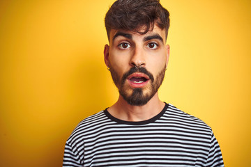 Obraz premium Young man with tattoo wearing striped t-shirt standing over isolated yellow background afraid and shocked with surprise expression, fear and excited face.