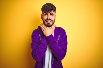 Obraz premium Young man with tattoo wearing sport purple sweatshirt over isolated yellow background shouting and suffocate because painful strangle. Health problem. Asphyxiate and suicide concept.