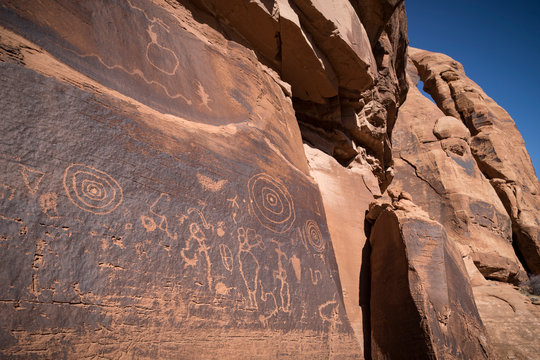 Native American petroglyphs etched onto sandstone rock wall below arch