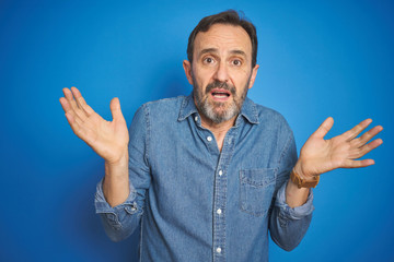 Handsome middle age senior man with grey hair over isolated blue background clueless and confused...