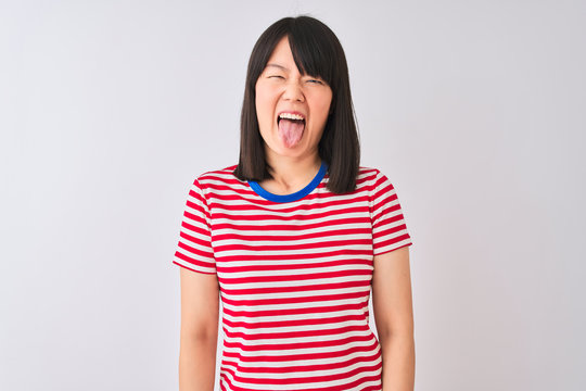 Young beautiful chinese woman wearing red striped t-shirt over isolated white background sticking tongue out happy with funny expression. Emotion concept.