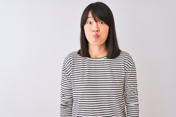 Young beautiful chinese woman wearing black striped t-shirt over isolated white background puffing...