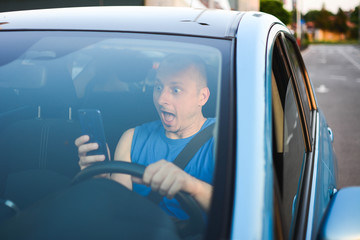 A man uses a smartphone while driving before sunset. Inside the car with smartphone. A man reads fake news over a smartphone while driving.