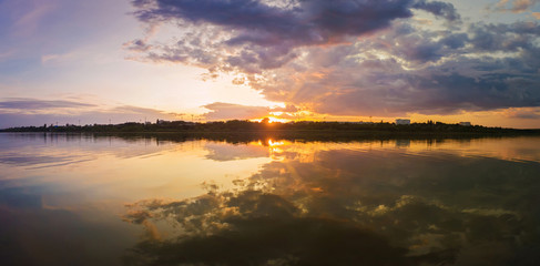 Wonderful sunset panorama over the city horizon with reflection on the calm lake water in a silent summer evening