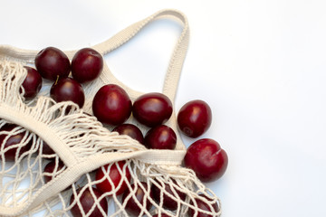 Plums in an ecological cotton reusable string bag, an alternative to plastic bags, on a white background. top view.