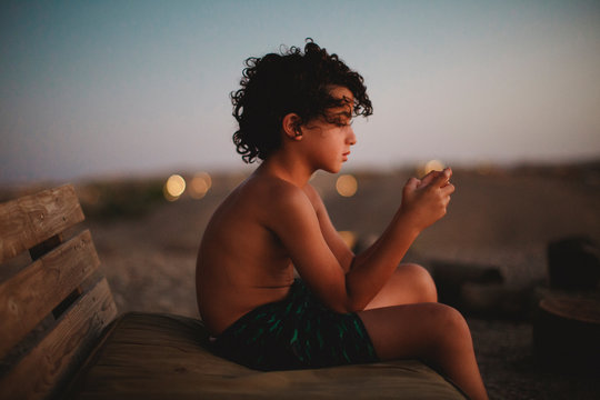 A young boy playing with his smartphone  in desert during sunset