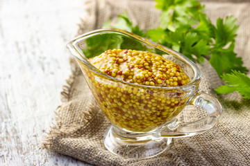 French grain mustard in a glass bowl on white wooden table.