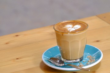 A cup of hot latte coffee on a blue saucer with a spoon and a piece of brown sugar,wooden dinning table at the cafe 