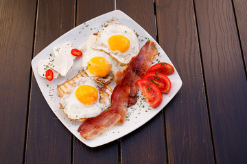 Healthy bacon fried egg on toast bread breakfast on plate , fresh tomatoes and cheese on plate , wood background.