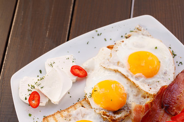 Healthy bacon fried egg on toast bread breakfast on plate , fresh tomatoes and cheese on plate , wood background.