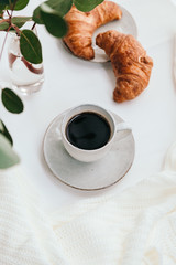 Cup of black coffee with croissant on white  table. The concept of breakfast, flat lay, top view.