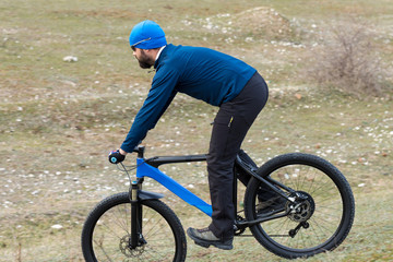 Cyclist in shorts and jersey on a modern carbon hardtail bike with an air suspension fork rides off-road on the orange-red hills at sunset evening in summer	