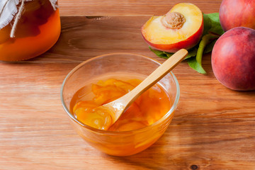 Piala with a spoon in homemade peach jam on a wooden round stand on the table in the morning sun. The concept of homemade conservation. Close up