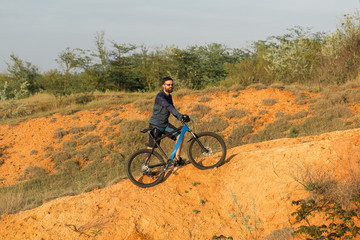 Cyclist in shorts and jersey on a modern carbon hardtail bike with an air suspension fork rides off-road on the orange-red hills at sunset evening in summer	