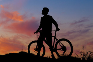 Obraz premium Cyclist in shorts and jersey on a modern carbon hardtail bike with an air suspension fork rides off-road on the orange-red hills at sunset evening in summer 