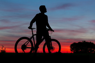 Obraz premium Cyclist in shorts and jersey on a modern carbon hardtail bike with an air suspension fork rides off-road on the orange-red hills at sunset evening in summer 