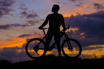 Obraz premium Cyclist in shorts and jersey on a modern carbon hardtail bike with an air suspension fork rides off-road on the orange-red hills at sunset evening in summer 