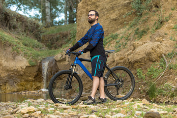 Fototapeta premium Cyclist in shorts and jersey on a modern carbon hardtail bike with an air suspension fork rides off-road on the orange-red hills at sunset evening in summer 