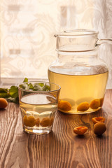 A glass cup and a jug with apricot fruit compote and ripe apricots on a wooden table. Sweet and healthy dessert. Copy space