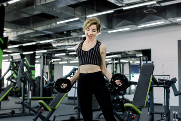 A young Caucasian sportswoman engaged in the gym, doing the exercise of leaning forward with a pancake for the bar.