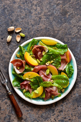 Fresh prosciut salad with peppers and pistachios on a concrete background. View from above.