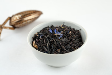 Dry black tea with blue flowers leaves in white bowl and metal tea spoon