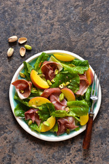 Fresh prosciut salad with peppers and pistachios on a concrete background. View from above.